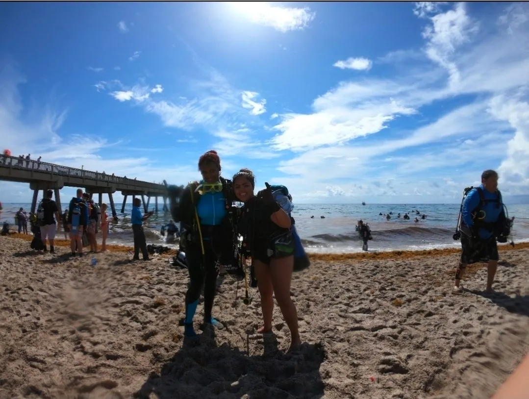 Divers in wetsuits on a beach beside a pier
